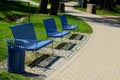 Park benches in light blue made of metal strips similar to a lattice. trash can and beautiful lawn with park paths of gravel thres