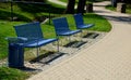 Park benches in light blue made of metal strips similar to a lattice. trash can and beautiful lawn with park paths of gravel thres