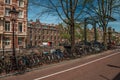 Park bicycles on street beside canal and old buildings in sunny day at Amsterdam. Royalty Free Stock Photo