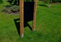 In the park, a chalk board is firmly anchored on the lawn with metal feet. wooden posts on both sides of the board