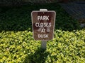 park closes at dusk sign and green plants