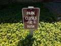 park closes at dusk sign and green plants