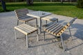 Park furniture chess table and chairs for four persons made of light metal and wooden beams with backrest on bright glade area gra Royalty Free Stock Photo