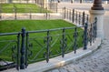 Park with a lawn behind a metallic decorative fence as a beige building in the background stands on the edge of a black pedestrian Royalty Free Stock Photo