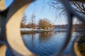 Park view trough a railing of a bridge over a lake.