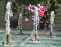 In a park with water a group of balloons float.