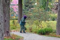 A park worker in a green suit and purple hood sweeps leaves with a broom.