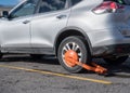 Parked car immobilized with orange parking clamp or boot Royalty Free Stock Photo