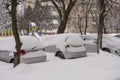 Parked cars, covered in snow, stand along the road. Snowfall in the city, falling snowflakes. Concept: traffic collapse, increased