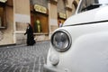 A parked Fiat 500 in the streets of Rome, a nun walking on the background. Royalty Free Stock Photo