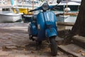 Small scooter in blue parked by a tree on the pier Royalty Free Stock Photo