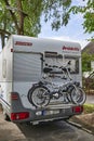 A parked white motorhome with a cycle carrier attached to the rear, with two bicycles