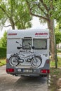 A parked white motorhome with a cycle carrier attached to the rear, with two bicycles