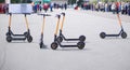 Parking lot with many free and affordable electric scooters for hire. City. Unrecognizable people in the background. Selective