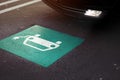 parking lot scene with car entering a section marked with symbol of a car with cable plug painted on ground.