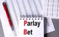 PARLAY BET text on notebook with pen, calculator and chart on grey background