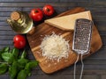 Parmesan cheese and grater on a cutting board. Whole and grated grana padano cheese, grater, olive oil, green basil and tomatoes