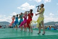 Girls in bright dresses sing on a wooden green stage during the ethnic Karatag festival on the shore of a Large lake