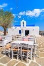 Tavern tables on square with typical white Greek church in Naoussa port, Paros island, Cyclades, Greece Royalty Free Stock Photo