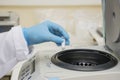 A part of an arm with labcoat and with blue nitril gloves putting a small plastic test tube in a micro centrifuge. Royalty Free Stock Photo