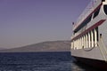 Part of big cruise liner in sea at sunny day. Cruise ship sailing from port. Skyline with mountains and ocean, horizon Royalty Free Stock Photo