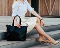 Part of body. Girl sitting on the stairs with a big black super fashionable handbag in a dress and Wide Fit Pointed Royalty Free Stock Photo