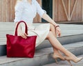 Part of body. Girl sitting on the stairs with a big red super fashionable handbag in a dress and Wide Fit Pointed Heels Royalty Free Stock Photo