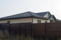 Part of a brick house with a gray tiled roof behind a brown fence Royalty Free Stock Photo