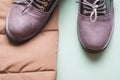 Part of brown autumn jacket and purple autumn pair of boots on light green background with copy space.