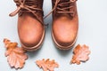 Part of brown autumn pair of boots on gray background with autumn oak leaves