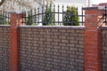 Part of a brown brick fence with black sharp iron rods