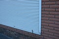 Part of a brown brick wall of a house with a door closed by white roller shutters Royalty Free Stock Photo