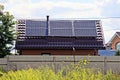 Part of a brown house with solar panels on the roof behind an iron fence in the grass