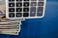 Part of calculator and dollars on a blue reflective background. Close-up. Royalty Free Stock Photo