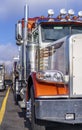 Part of classic big rig orange semi truck with chrome accessories stand in line on truck stop