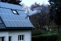 Part of cozy white house in winter in European village, solar panels installed on roof, smoke comes from chimney, autonomous