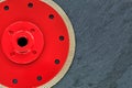 A part of a diamond cutting wheel is red with a threaded nut on a background of gray granite