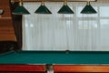 Part of an empty billiard table and lamps above it