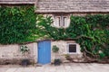 Part of exterior of old house of light brick with tiled roof and low blue door. The facade of the house are entwined with green iv Royalty Free Stock Photo