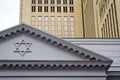 Part of the facade of the synagogue with the Star of David against the backdrop of a modern high-rise building made of glass and