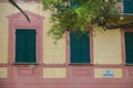 Part of the facade of an Yellow and pink italian building with windows with green shutters.