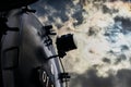 Part of the front of a black historic locomotive with a dark sky made of dramatic clouds and a hidden sun