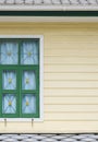 Green window on yellow wooden wall with gray tile roof of vintage 2 story house in vertical frame