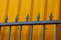 Part of the iron fence of black sharp rods against the background of the yellow wall Royalty Free Stock Photo