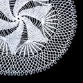 A part of isolated crocheted white doily with a pattern of spiral and fans on a black background. Round decorative doily