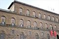 Part of the large facade, with three banners on the roof and entrance, of Palazzo Pitti in Florence.