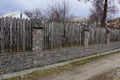 Part of an old rural fence made of stones and gray sharp logs outside in the grass