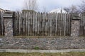 Part of an old rural fence made of stones and gray sharp logs outside in the grass