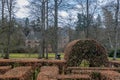 Part of a maze made up of brown leaf bushes with bare trees and the Het Oude Loo castle in the background