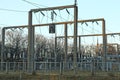 Part of a power plant with poles, transformers and wires behind a fence